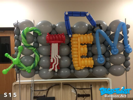 A balloon display spells out “STEM” using colorful balloons. Each letter is themed: S in green like DNA, T in red like a circuit board, E in yellow like building blocks, and M in blue with gears. The background is made of gray balloons.