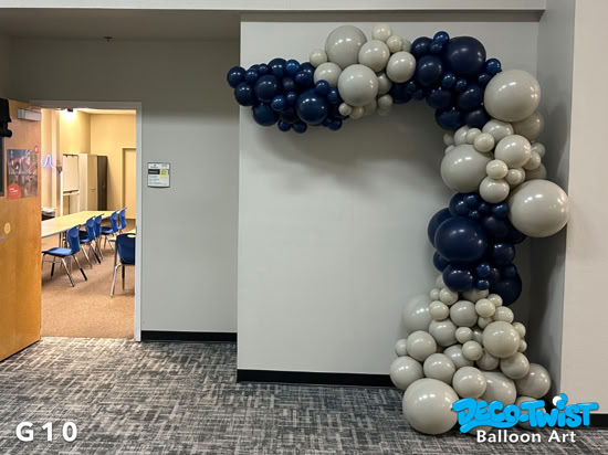 A balloon garland in navy blue and gray tones is arranged around the corner of a wall, forming an archway that frames the space with a modern, elegant look.