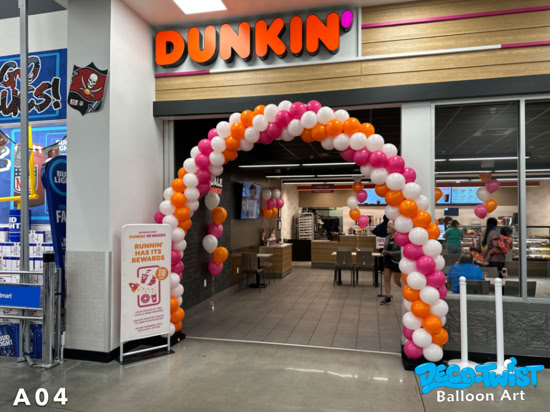 A balloon arch in orange, pink, and white stands at the entrance of a Dunkin’ store, creating a festive display for customers walking in during their grand opening celebration.