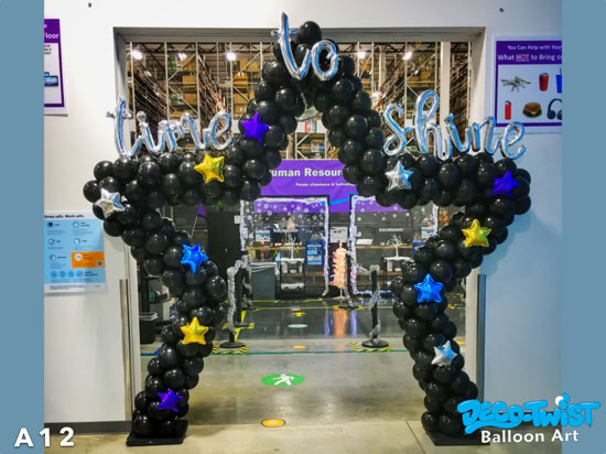 A balloon arch shaped like a star is made of black balloons and decorated with shiny metallic star balloons in gold, blue, purple, and silver. At the top, glittery silver balloon letters spell out “time to shine,” creating a bold and celebratory entrance display.